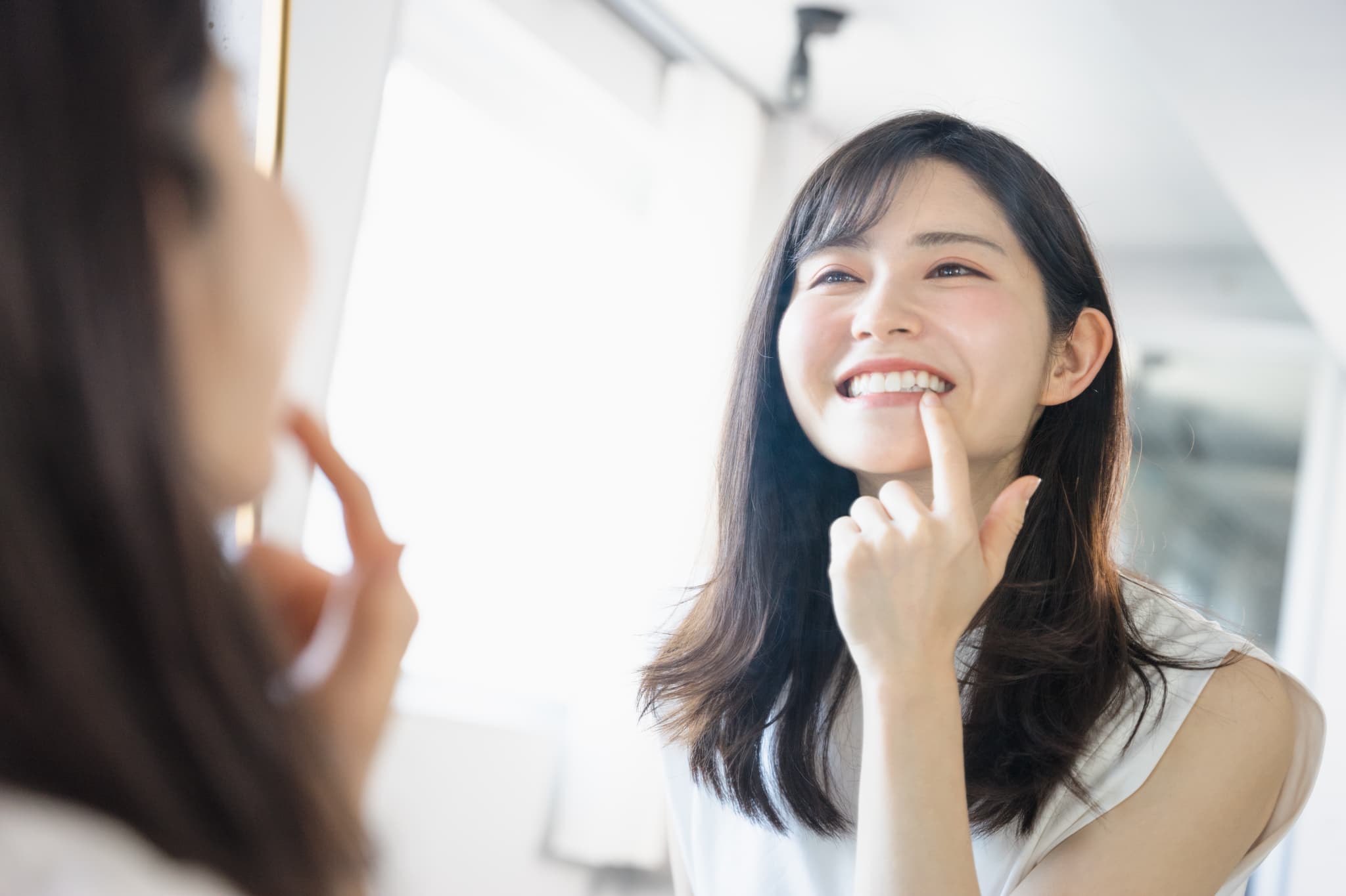 ホワイトニングで歯がもろくなってないか鏡で歯を見る女性