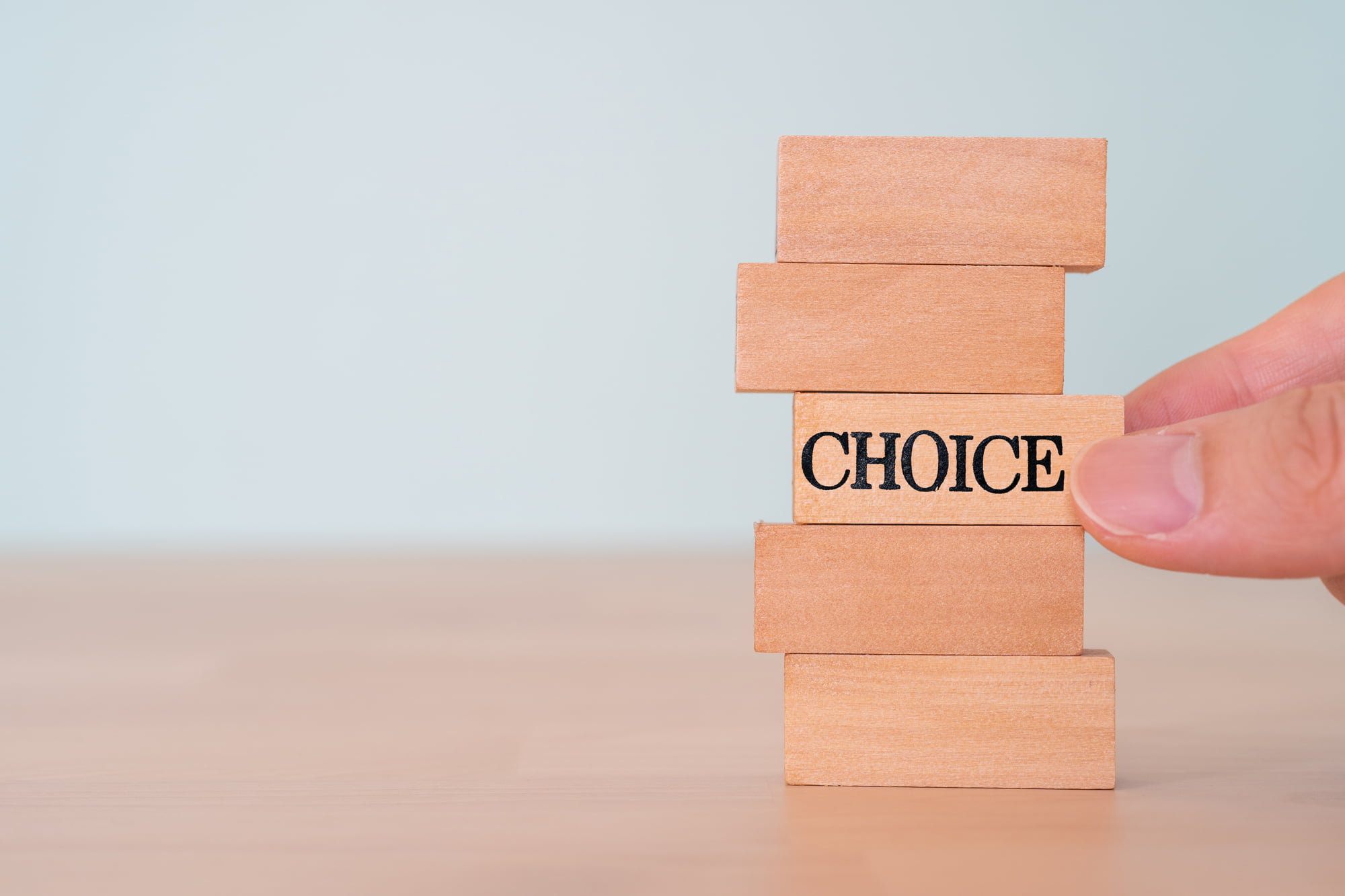 積まれたブロックの真ん中からCHOICEと書かれたブロックを抜き取ろうとしている指
